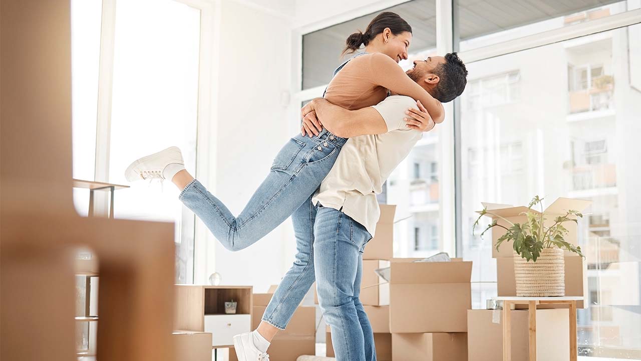 Jovem casal em um apartamento cheio de caixas de papelão celebrando a conquista da casa própria